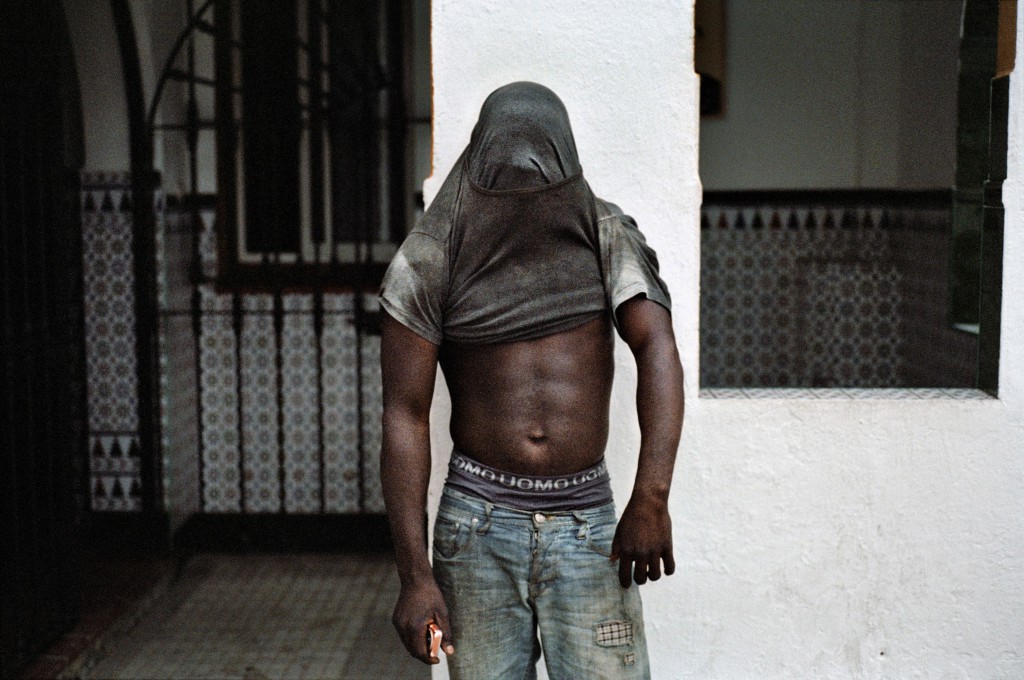 Photographie en couleur d'un migrant africain le visage caché par son tee-shirt.